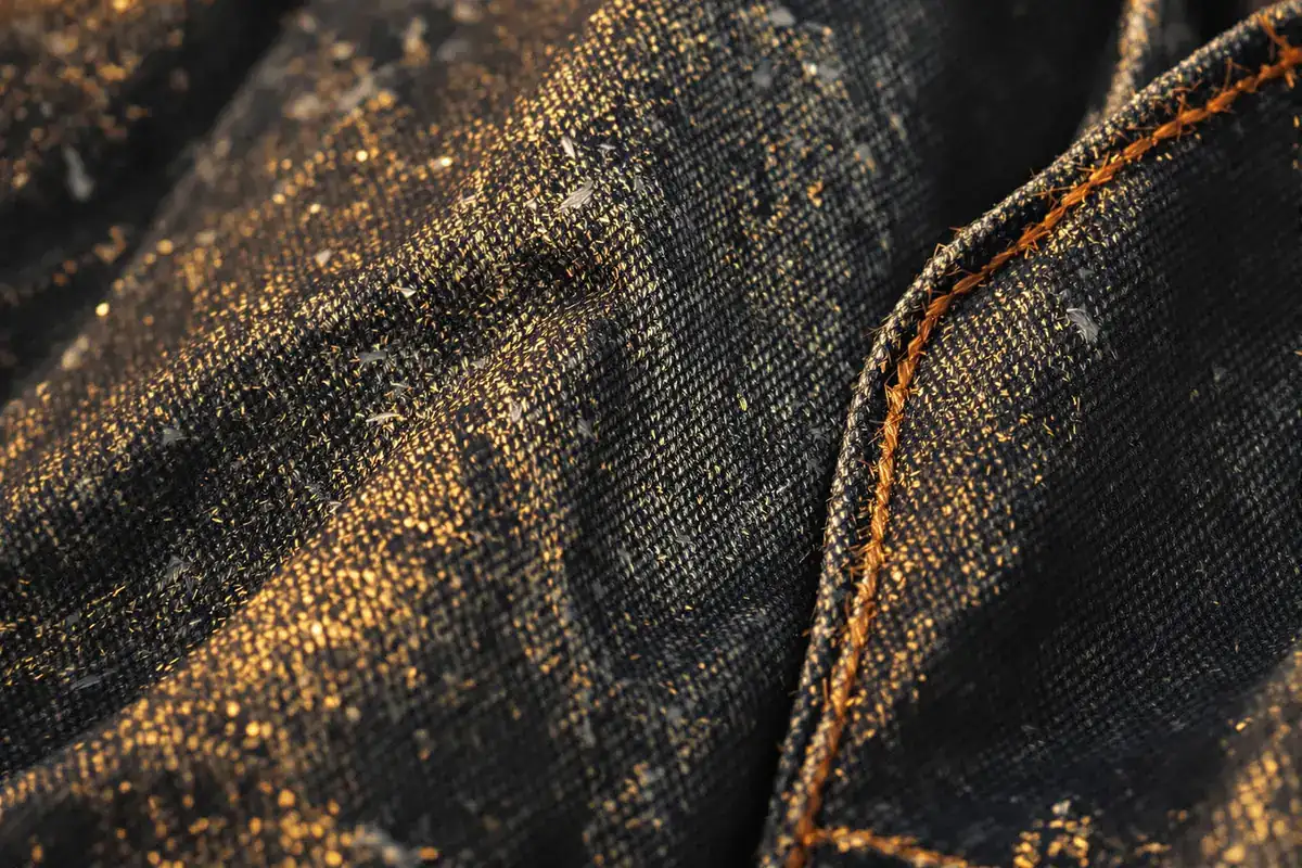 Gros plan sur un denim sombre haut de gamme et sa surpiqûre orangée dans une lumière dorée